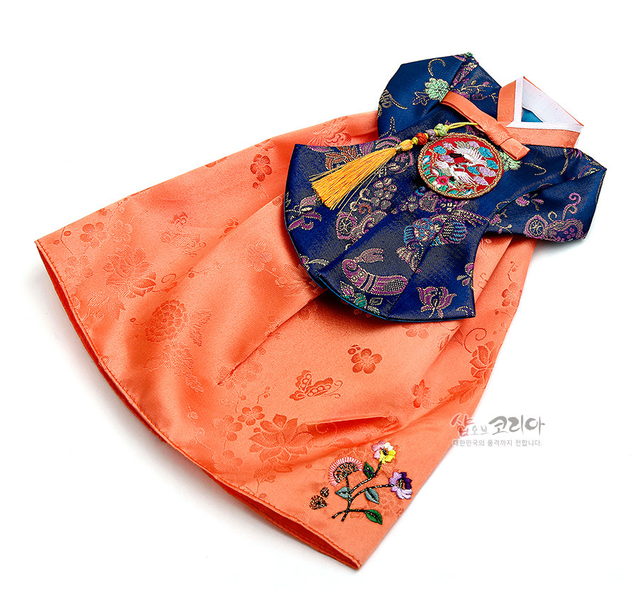 [텍스트: 샵오브코리아 대한민국의 품격까지 전합니다] 주홍색 비단 치마와 남색 비단 당의 상의로 이루어진 와인커버, 꽃과 나비 문양 자수와 원형 학 수자수, 노란 술 노리개 장식이 돋보이는 전통 한복 형식 디자인