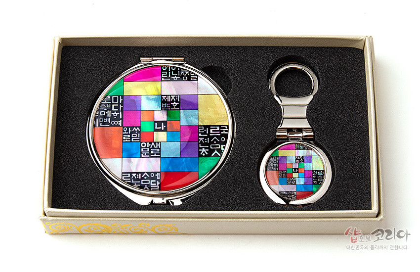 [텍스트: 나] 자개 상감 기법의 금속 손거울과 키링 세트, 다채로운 오방색 조각보 바탕 위 훈민정음 자모 문양이 배치된 디자인