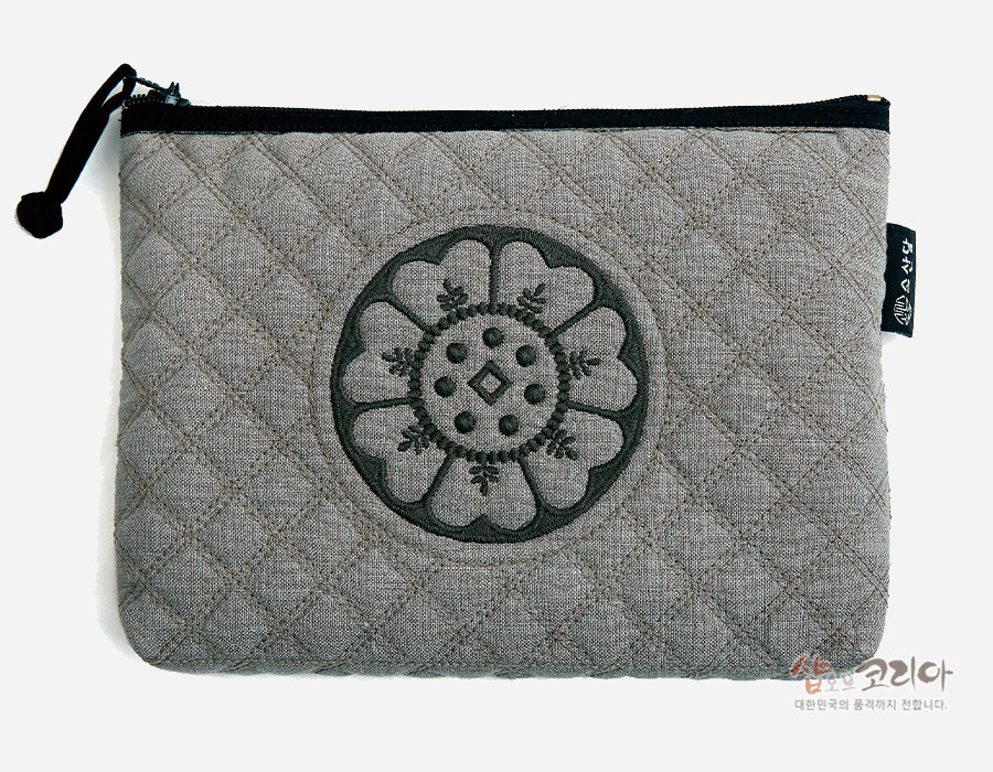 [텍스트: 샵오브코리아 대한민국의 품격까지 전합니다.] 회색 누비 원단 위에 흑색 백제 수막새 연꽃 문양 자수 장식, 상단 검정 지퍼와 끈 디테일의 직사각 파우치 디자인