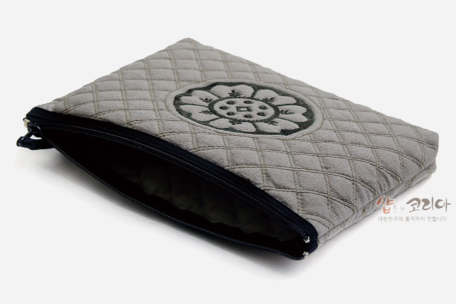 [텍스트: 샵오브코리아 대한민국의 문화가치 살립니다] 회색 누빔 패브릭에 흑색 백제 수막새 연꽃 문양 자수를 중심 배치한 지퍼 파우치 디자인