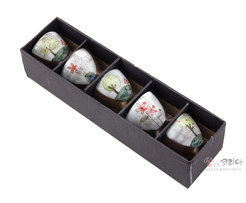 [텍스트: 샵오브코리아 대한민국의 품격까지 전합니다.] 갈색 도자기 재질 삼각 다리 소주잔에 흰 바탕, 수채화풍 나무와 집, 꽃, 잎 야생화 풍경 문양이 그려진 세트 모습