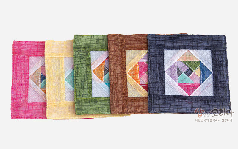 [텍스트: 샵오브코리아 대한민국의 품격까지 전합니다.] 오방색 계열 모시 천으로 제작된 사각 컵받침, 중앙에 다양한 색 모시 조각을 기하학적 조각보 패치워크 기법으로 배치한 전통 문양 장식