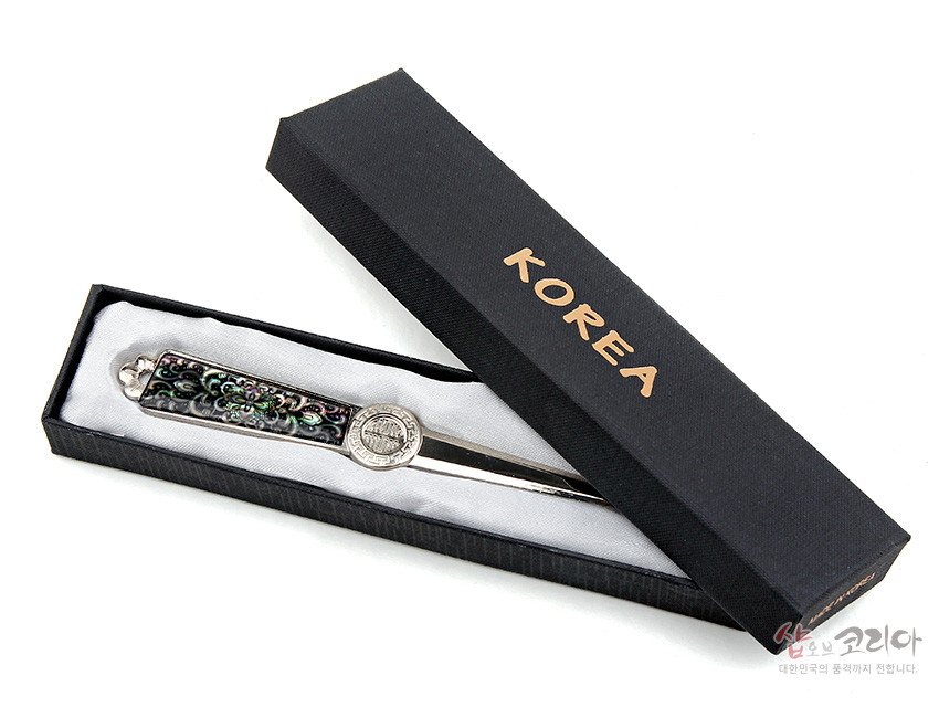 [텍스트: KOREA, 샵오브코리아 대한민국의 품격까지 전합니다] 흑색 케이스 속 은색 금속 편지칼에 자개 상감 당초문과 원형 전통 문양 장식이 돋보이는 디자인