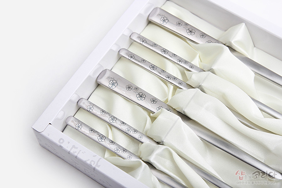 [텍스트: 샵오브코리아 대한민국의 품격까지 전합니다] 은색 스테인리스 재질, 손잡이 부분에 섬세한 매화 문양이 음각된 젓가락과 숟가락 2인 수저 세트 진열 이미지