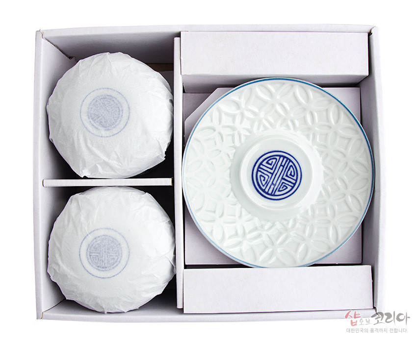 [텍스트: 샵오브코리아 대한민국의 품격까지 전합니다.] 백자 재질에 청색 길상문 원형 문양과 연꽃잎 기하학 투각무늬가 조화를 이룬 2인용 찻잔 받침 구성 이미지