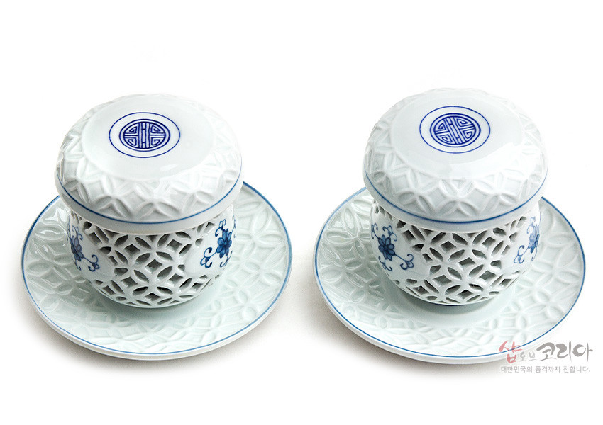 [텍스트: 샵오브코리아 대한민국의 품격까지 전합니다.] 백자 재질에 투각 기법으로 격자무늬를 낸 2인 다기잔세트, 청색 길상문과 꽃문양, 연한 청자색 양각 문양 받침 접시 구성