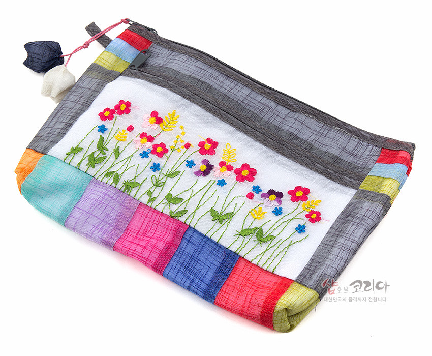 [텍스트: 샵오브코리아, 대한민국의 품격까지 전합니다.] 흑색 모시 바탕에 다채로운 색실로 들꽃 야생화 자수 장식, 오방색 모시 조각을 누빔 배치한 지퍼 파우치형 디자인