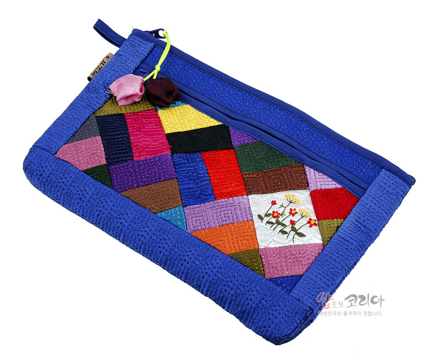 [텍스트: 샵오브코리아 대한민국의 품격까지 전합니다.] 청색 누비천 테두리에 다채로운 비단 조각보 패치워크와 꽃 자수 문양이 어우러진 지퍼형 파우치 디자인
