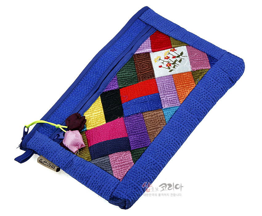 [텍스트: 샵오브코리아 대한민국의 품격까지 전합니다.] 청색 누비 천 위에 다채로운 색비단 조각보 패치워크와 흰색 바탕 꽃 자수 문양이 조화를 이루는 지퍼형 파우치 디자인