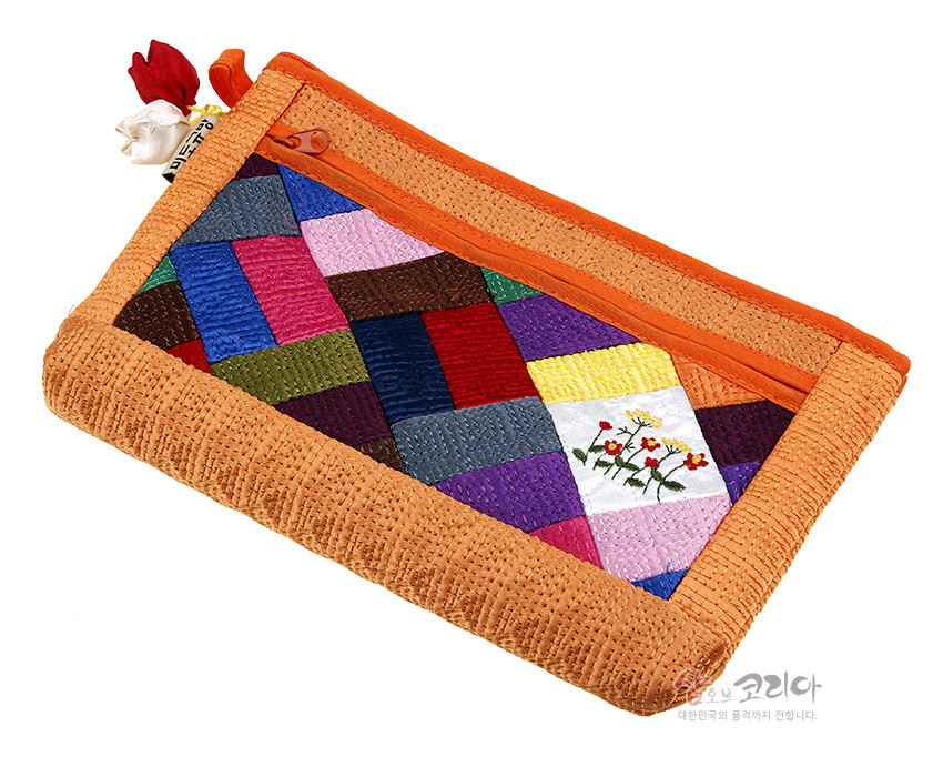 [텍스트: 샵오브코리아 대한민국의 품격까지 전합니다.] 오렌지색 누비 천 바탕에 비단 조각보 패치워크와 꽃자수 장식, 조개 모양 노리개 매듭 장식을 더한 파우치 이미지 설명
