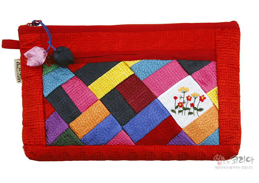 [텍스트: 샵오브코리아 대한민국의 품격까지 전합니다] 붉은 비단 누비 바탕에 다채로운 조각보 패치워크와 꽃 자수, 연분홍·남색 매듭 장식이 달린 지퍼형 파우치 모습
