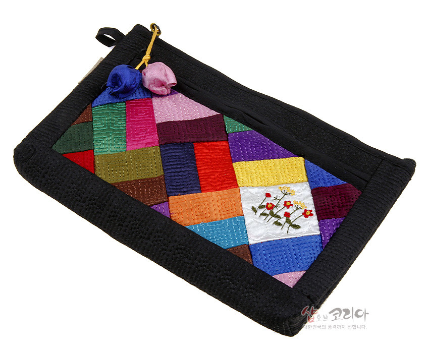 [텍스트: 샵오브코리아 대한민국의 품격까지 전합니다.] 흑색 누비 천 위에 다채로운 비단 조각보 패치워크와 흰색 조각의 꽃 자수, 매듭 장식이 더해진 직사각형 파우치 디자인