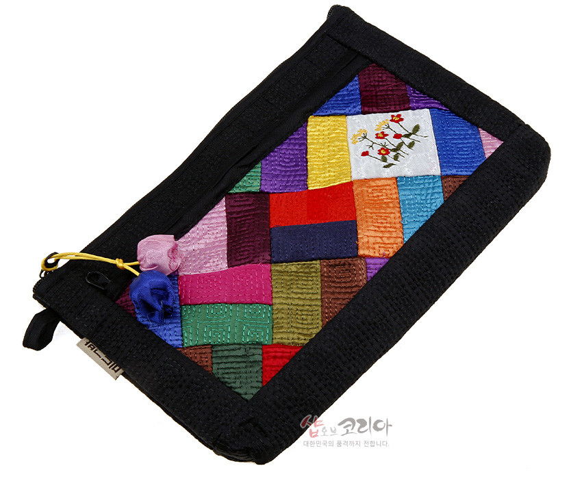 [텍스트: 샵오브코리아 대한민국의 품격까지 전합니다.] 흑색 누비 바탕에 다채로운 비단 조각보 패치워크와 흰색 조각 위 꽃 자수 문양, 색동 매듭 장식이 어우러진 직사각 파우치 디자인