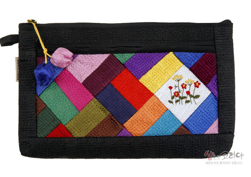[텍스트: 샵오브코리아 대한민국의 품격까지 전합니다.] 흑색 바탕 누비 원단에 다채로운 비단 조각보 패치워크와 흰색 면의 꽃 자수, 양단 장미 매듭 장식이 어우러진 직사각형 파우치 디자인