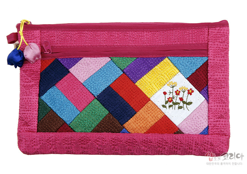 [텍스트: 샵오브코리아 대한민국의 품격까지 전합니다.] 진분홍 누비 바탕 위 다채로운 색상 조각보 패치워크와 흰색 면의 꽃 자수, 실크 매듭 장식 지퍼가 어우러진 직사각형 파우치 디자인