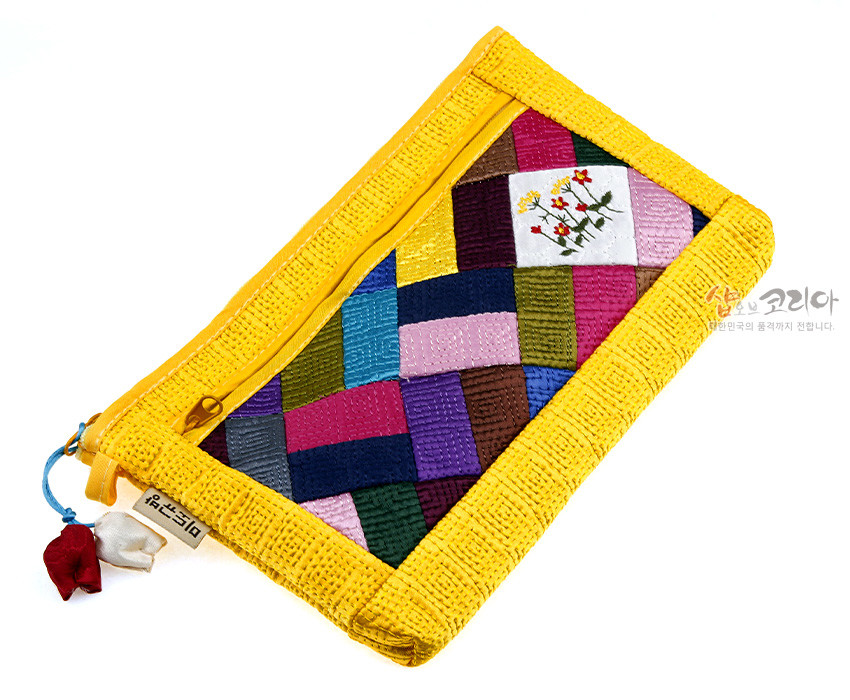 [텍스트: 샵오브코리아] 노란색 누비 원단 위 다색 조각보 패턴과 흰 바탕 꽃 자수 장식이 조화를 이루는 패브릭 파우치 모습