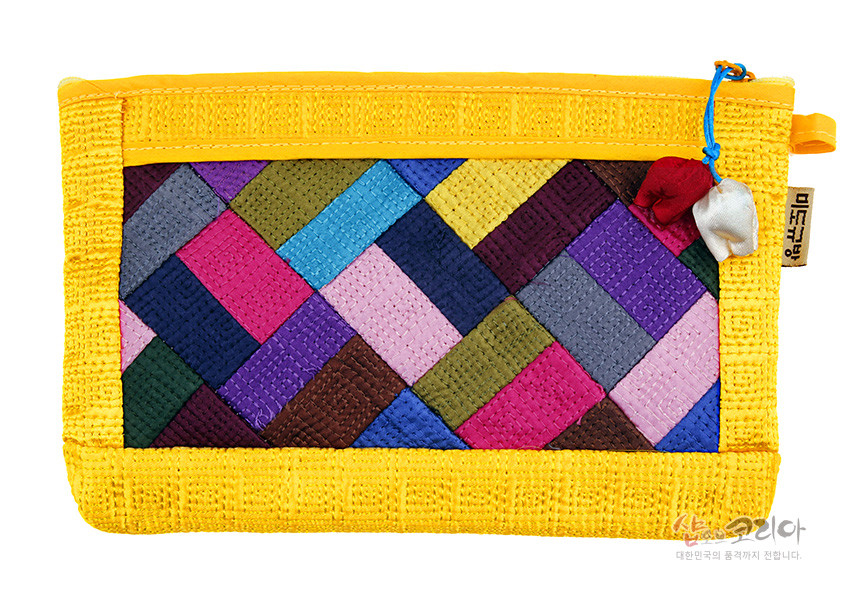 [텍스트: 미소쿠망, 샵코리아 대한민국의 품격까지 전합니다.] 노란색 누비 천을 바탕으로 다양한 색상의 조각보 패턴을 더한 파우치, 지퍼에 매단 빨강·흰색 복주머니 장식 포인트인 디자인