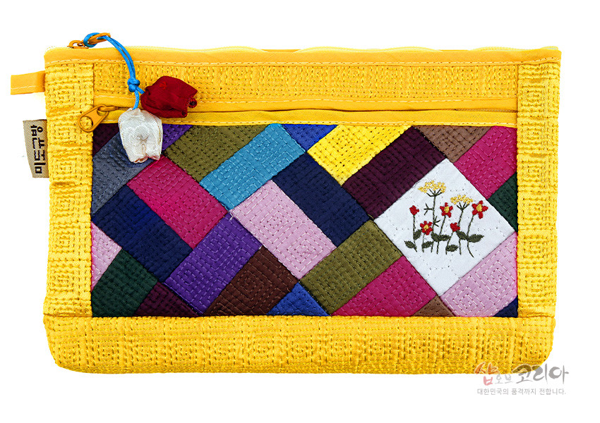 [텍스트: 샵오브코리아] 노란 누비 원단 바탕에 다채로운 색상의 조각보 패턴과 흰색 바탕 꽃 자수 문양, 매듭 장식이 더해진 파우치 디자인