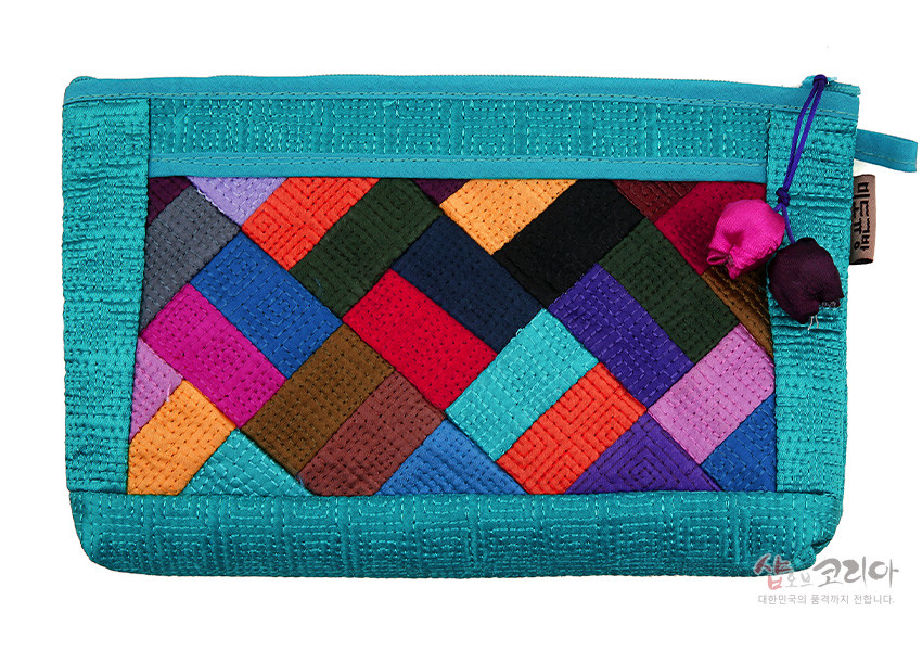 [텍스트: 샵오브코리아 대한민국의 품격까지 전합니다.] 하늘색 누비천에 다채로운 조각보 패치워크가 어우러진 직사각형 지퍼 파우치, 옆면 복주머니 장식 디테일 강조한 구성