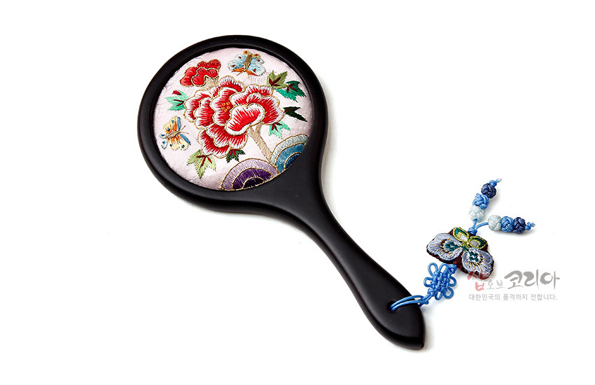 [텍스트: 샵오브코리아 대한민국의 품격까지 전달합니다.] 연분홍 비단 위 붉은 모란과 나비 자수 장식 원형 손거울, 흑색 손잡이와 청색 매듭·나비 자수 장식 구성