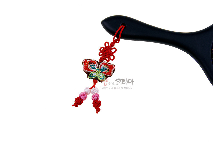 [텍스트: 샵오브코리아 대한민국의 멋과 정까지 전합니다.] 검은색 손잡이에 붉은 끈으로 매단 다홍색 나비 자수 장식과 매듭, 분홍·백색 구슬 장식 구성