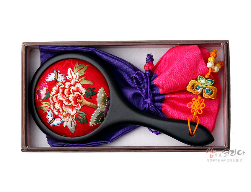 [텍스트: 샵오브코리아 대한민국의 품격까지 전합니다.] 붉은 비단 바탕에 모란과 나비 자수를 놓은 원형 손거울과 보라·분홍 비단 복주머니, 매듭 노리개 장식 세트 이미지
