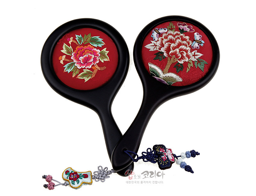 [텍스트: 샵오브코리아 대한민국의 품격까지 전합니다.] 붉은 비단 바탕에 모란과 나비 자수 장식된 원형 손거울, 검은 손잡이와 매듭 노리개 술 장식 구성