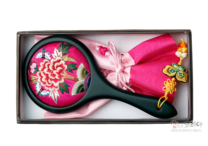 [텍스트: 샵오브코리아 대한민국의 품격까지 전합니다.] 분홍 비단 바탕 모란꽃·나비 자수 장식 손잡이 거울과 배색 비단 주머니, 나비 매듭 술 장식 구성 이미지