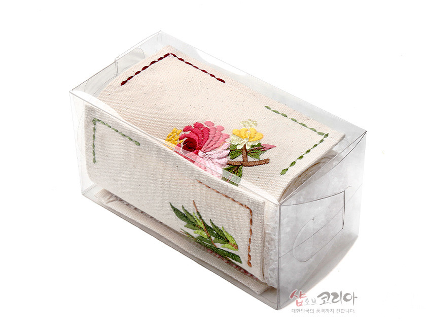 [텍스트: 샵오브코리아 대한민국의 품격까지 전합니다.] 투명 플라스틱 케이스에 담긴 광목 식탁보, 사군자 풍 꽃과 잎 자수, 가장자리 스티치 장식 디자인
