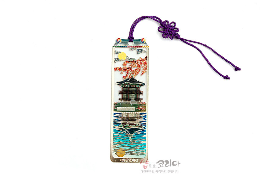 [텍스트: 샵오브코리아 대한민국의 품격까지 전합니다.] 금속 재질 위에 궁과 향원정을 섬세한 채색으로 표현하고, 벚꽃과 호수 문양을 더한 직사각형 책갈피와 보라색 전통 매듭끈 장식