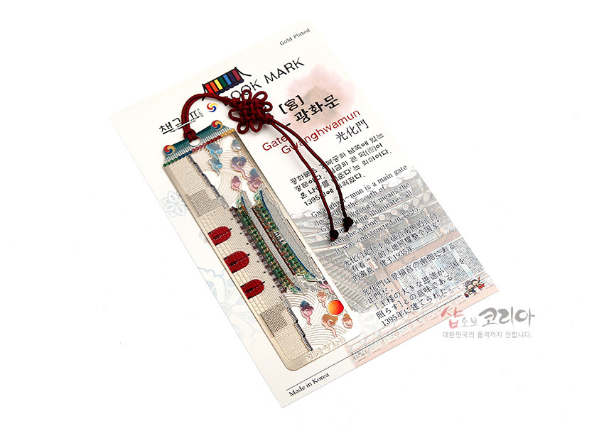 [텍스트: BOOK MARK, Gate of Gyeonghwamun, 광화문, Made in Korea] 금속 재질 위에 광화문 전경과 구름, 해 문양을 섬세한 채색으로 표현하고 붉은 전통 매듭 끈을 더한 직사각 책갈피형 디자인