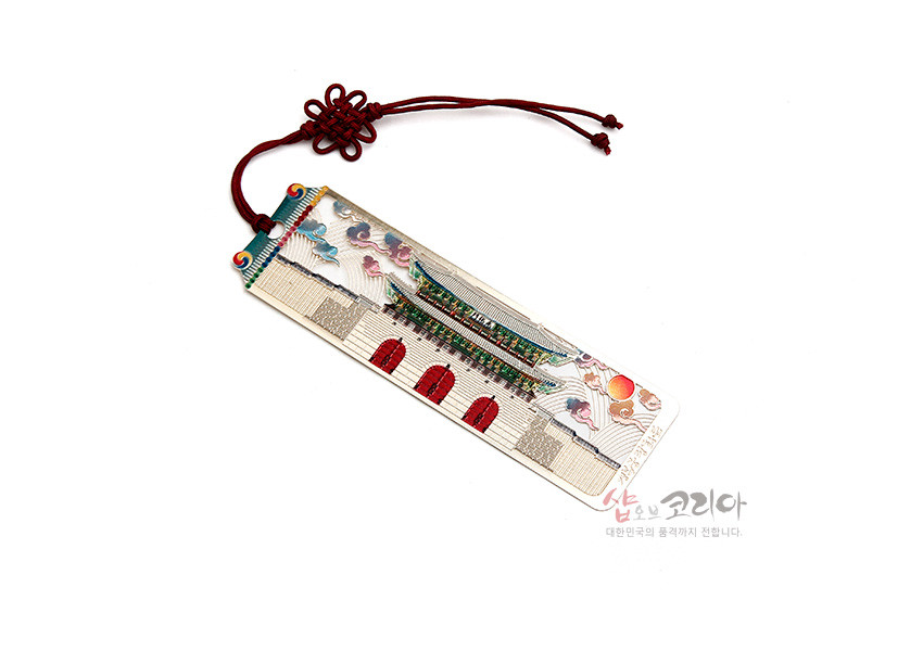 [텍스트: 샵오브코리아 대한민국의 품격까지 전합니다.] 금속 재질 직사각 책갈피에 광화문과 오방색 구름, 해 문양을 섬세한 채색으로 표현하고 붉은 전통 매듭 끈으로 마감한 디자인