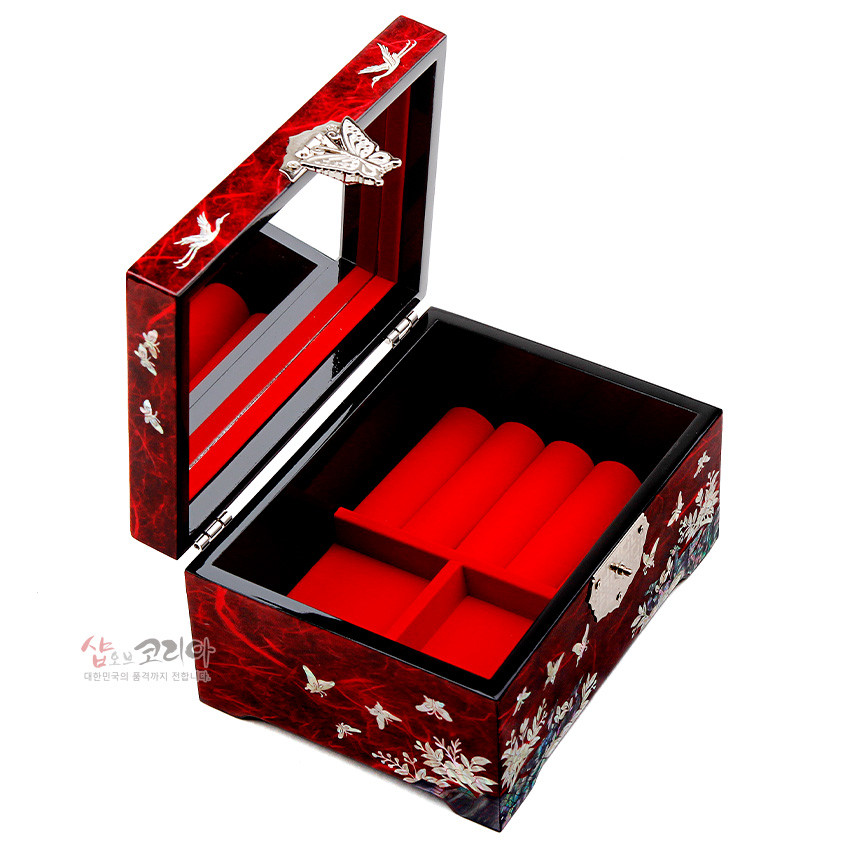 [텍스트: 샵오브코리아 대한민국의 문화 꽃까지 전하는 마음] 적색 옻칠 한지 바탕 위 자개 상감으로 학과 나비, 매화·산수 문양을 장식하고 내부는 붉은 벨벳 칸막이로 구성된 직사각 보석함 이미지 설명