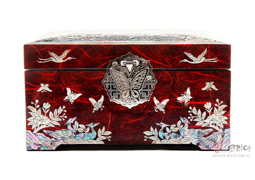 [텍스트: 샵오브코리아 대한민국의 품격까지 전합니다.] 적색 한지 바탕 위 자개 상감 기법으로 송학과 매화, 나비, 연못 풍경을 섬세하게 표현한 직사각 옻칠 보석함 디자인