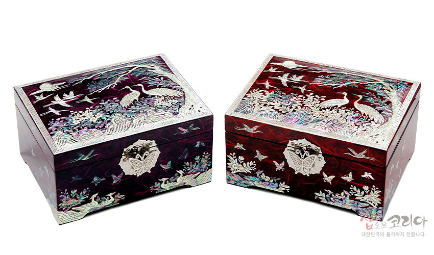 [텍스트: 샵오브코리아 대한민국의 품격까지 전합니다.] 적색 옻칠 바탕 위 진채색 자개 상감으로 송학과 소나무, 나비, 산수 문양을 정교하게 표현한 직사각 한지 보석함 모습