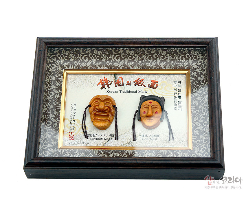 [텍스트: Korean Traditional Mask, Yangban Mask, Bune Mask, MADE IN KOREA] 어두운 나무 액자에 금빛 내곽을 두르고, 당초문 양단 바탕 위에 황갈색 하회 양반탈과 부네탈 미니어처를 입체 배치한 구성