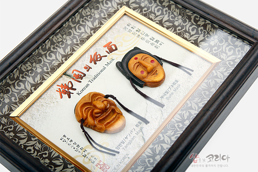 [텍스트: Korean Traditional Mask, MADE IN KOREA, 양반탈 Yangban Mask, 부네탈 Bune Mask] 당초무늬 은회색 문양 배경에 황갈색 나무 하회탈 미니어처와 금색 내틀, 짙은 목재 액자의 입체 장식 구성