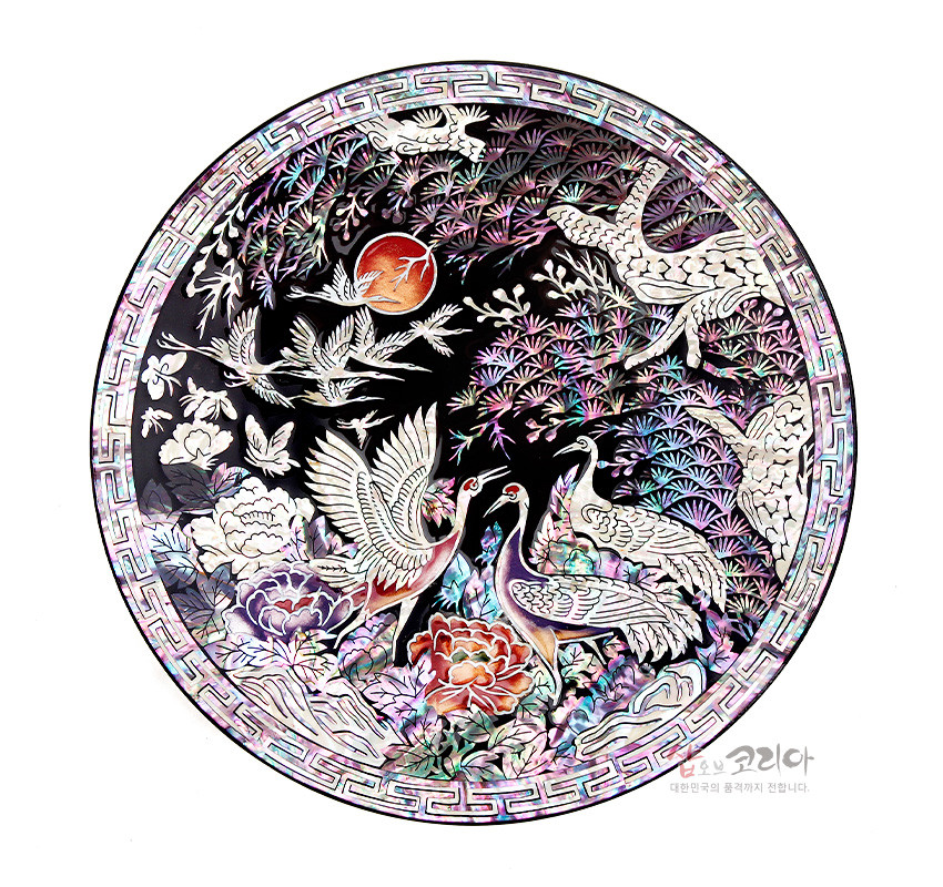 [텍스트: 샵오브코리아 대한민국의 품격까지 전합니다.] 흑색 옻칠 바탕 위 자개 상감 기법으로 송학, 소나무, 해와 연꽃·모란 문양을 다채로운 오방색 계열로 표현한 원형 쟁반형 나전칠기 오브제