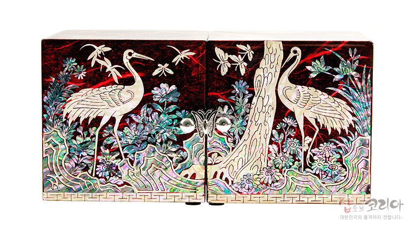 [텍스트: 샵오브코리아 대한민국의 혼까지 전합니다.] 붉은 옻칠 바탕 위 자개 상감 기법으로 송학과 소나무, 나비와 꽃, 기하학적 문양을 섬세하게 장식한 한지 쌍합 정면 장식 이미지 표현