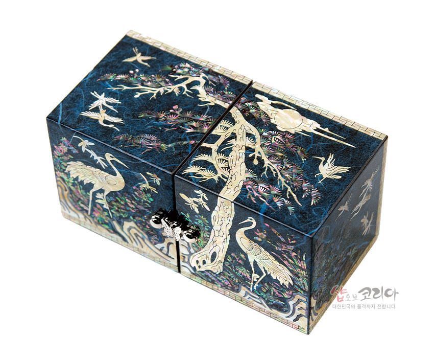 [텍스트: 샵오브코리아 대한민국의 품격까지 전합니다.] 청색 옻칠 바탕 위 자개 상감 기법으로 소나무와 학, 구름과 수목 문양을 정교하게 표현한 직사각형 한지 쌍합 보석함 디자인