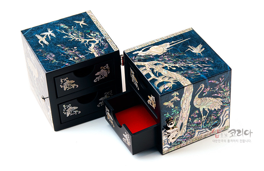 [텍스트: 샵오브코리아 대한민국의 품격까지 전합니다] 청색 한지 바탕 위 자개 상감으로 소나무와 학, 구름과 달을 섬세하게 표현한 직사각 쌍합 보석함, 붉은 색 내피 대비가 돋보이는 전통 나전칠기 공예품 묘사