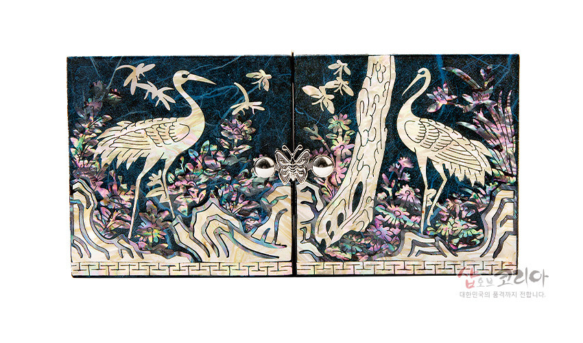 [텍스트: 샵오브코리아 대한민국의 품격까지 전합니다] 청색 한지 위 자개 상감 기법으로 소나무와 학, 구름과 꽃무늬를 섬세하게 표현한 직사각형 쌍합 보석함 정면 장식 이미지