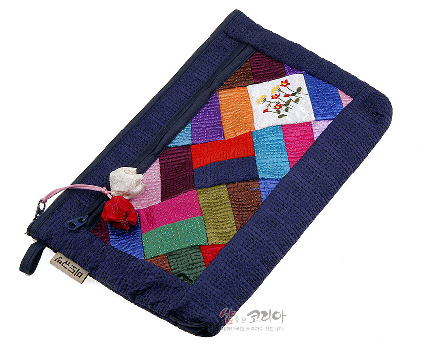[텍스트: 샵오브코리아] 남색 누비 천을 바탕으로 알록달록한 조각보 패치워크와 흰 바탕 꽃자수 장식, 매듭 달린 지퍼가 있는 직사각형 파우치 이미지