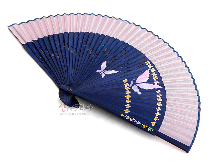 [텍스트: 샵오브코리아 대한민국의 품격까지 전합니다.] 남색 대와 분홍색 실크 접선에 나비와 노란 꽃 문양을 수공 채색한 한국 전통 실크 부채 모습