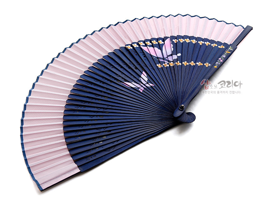 [텍스트: 샵오브코리아 대한민국의 품격까지 전합니다.] 남색 대와 분홍색 실크 부채살 조합, 수공 나비와 노랑 꽃문양이 그려진 전통 접부채 디자인
