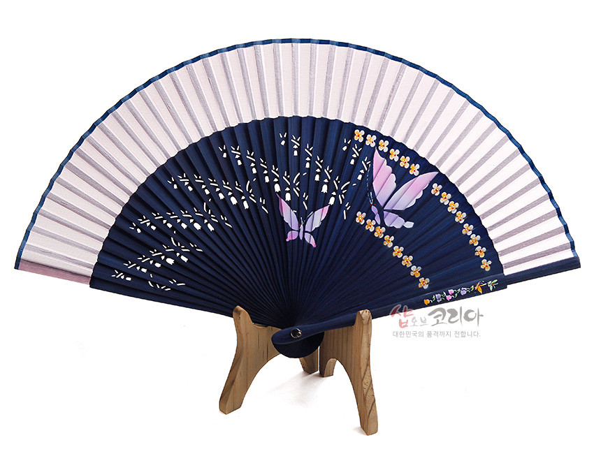 [텍스트: 샵오브코리아 대한민국의 품격까지 전합니다.] 남색 대와 분홍빛 실크 선면에 나비와 노란 꽃문양이 수공으로 그려진 전통 접이식 부채 디자인
