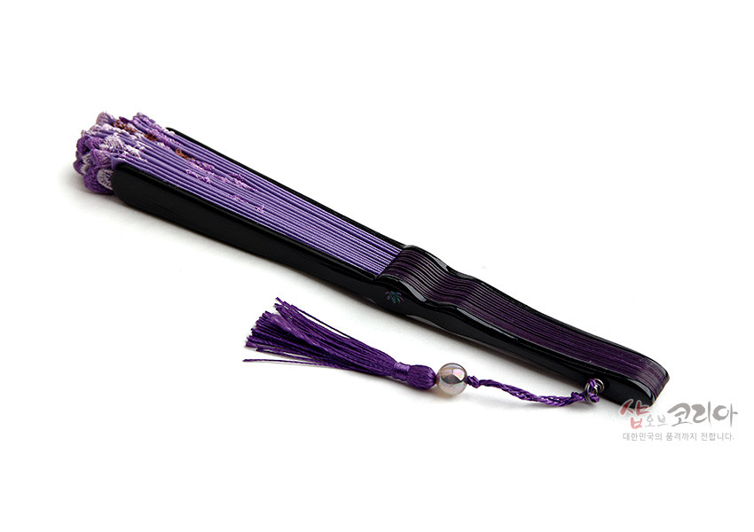 [텍스트: 샵오브코리아 대한민국의 품격까지 전합니다.] 자주색과 연보라색이 조화된 비단선, 검정색 나무살과 구슬 장식 술로 꾸민 전통 접이부채 이미지 설명