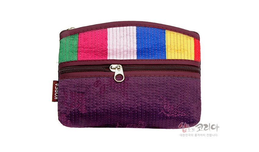 [텍스트: KOREA, 샵오브코리아 대한민국의 품격까지 전합니다.] 자주색 바탕 위 세로 누비선과 상단 오방색 색동 천 장식, 중앙 지퍼 여밈이 있는 직사각형 천 소재 동전 파우치형 지갑 이미지 설명