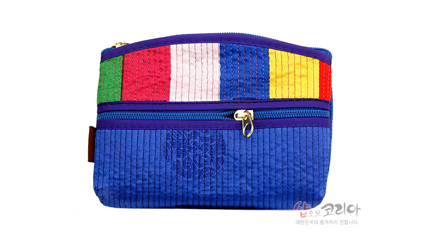 [텍스트: 샵오브코리아 대한민국의 품격까지 전합니다.] 청색 누비천 바탕에 전면 세로 누비선, 상단에 녹색·적색·백색·청색·황색 색동 천을 덧댄 황동 지퍼 장식 직사각형 파우치형 동전지갑 이미지 설명