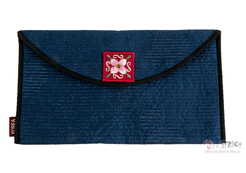 [텍스트: KOREA] 짙은 남색 전통 누비 비단으로 제작된 봉투형 지갑, 중앙 붉은 바탕 위에 분홍 꽃자수 문양이 놓인 디자인